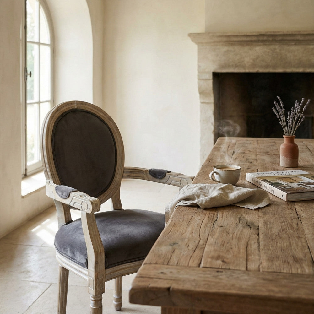 Poltrona Constance con braccioli in un ambiente living elegante, vicino a un tavolo in legno con tazza di caffè fumante e camino sullo sfondo.