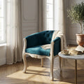 Poltrona Coreen in velluto blu e legno ambientata in un salotto luminoso con pavimento in parquet.