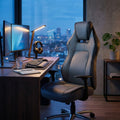 Poltrona da gaming GTA in poliuretano grigio chiaro ambientata in uno studio serale con vista città.