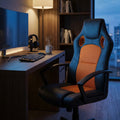 Poltrona da ufficio Uncharted in poliuretano nero e arancione, ambientata in uno studio serale con illuminazione calda e monitor acceso.