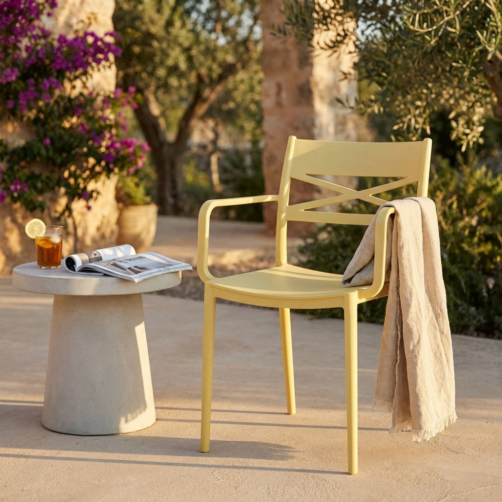 Poltrona Darleen in polipropilene giallo ambientata in un patio esterno con tavolino in cemento.