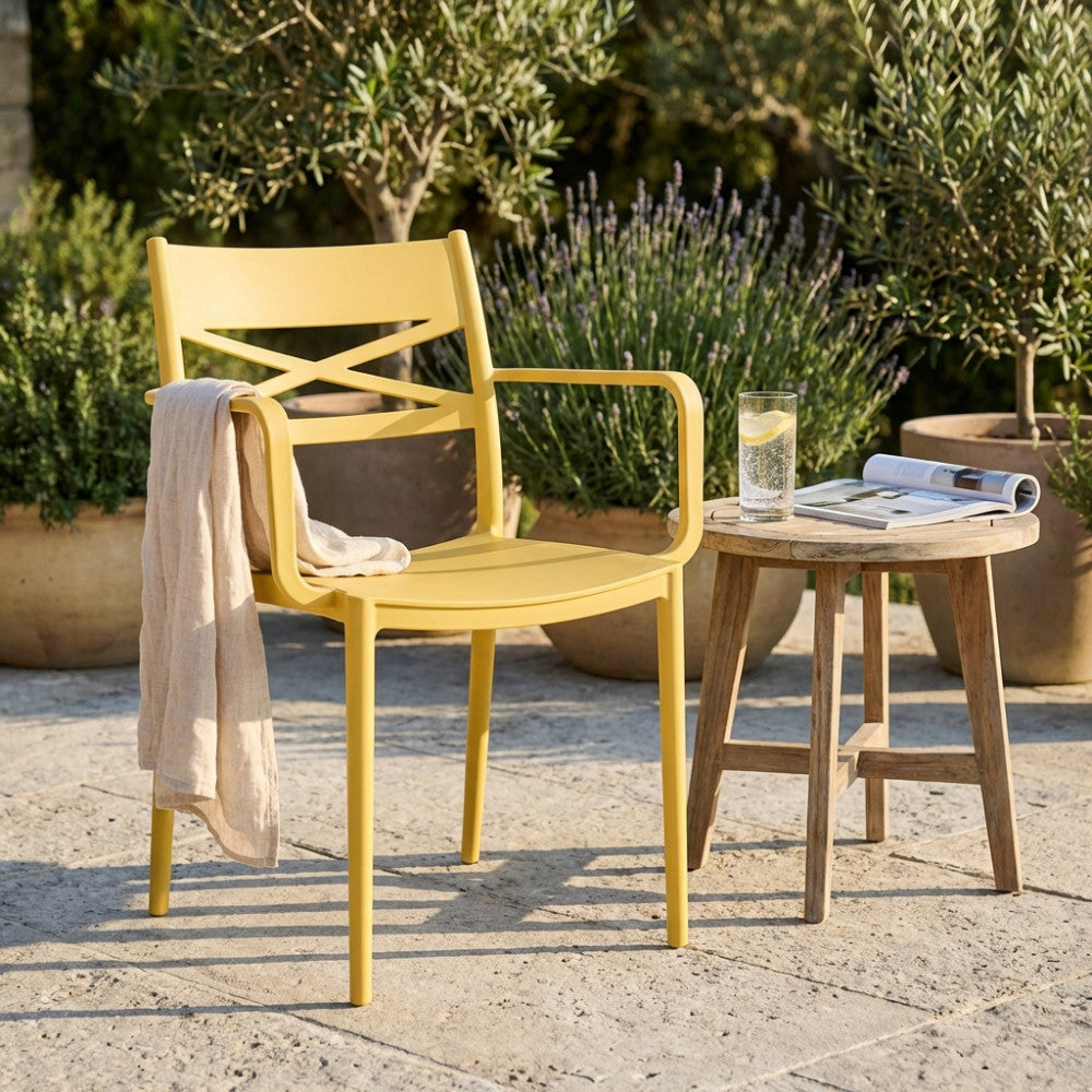 Sedia con braccioli Darleen gialla affiancata a un tavolino in legno in un giardino soleggiato.