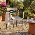 Poltrona Darleen in polipropilene grigio scuro ambientata in un giardino rustico con pavimento in pietra e piante fiorite.