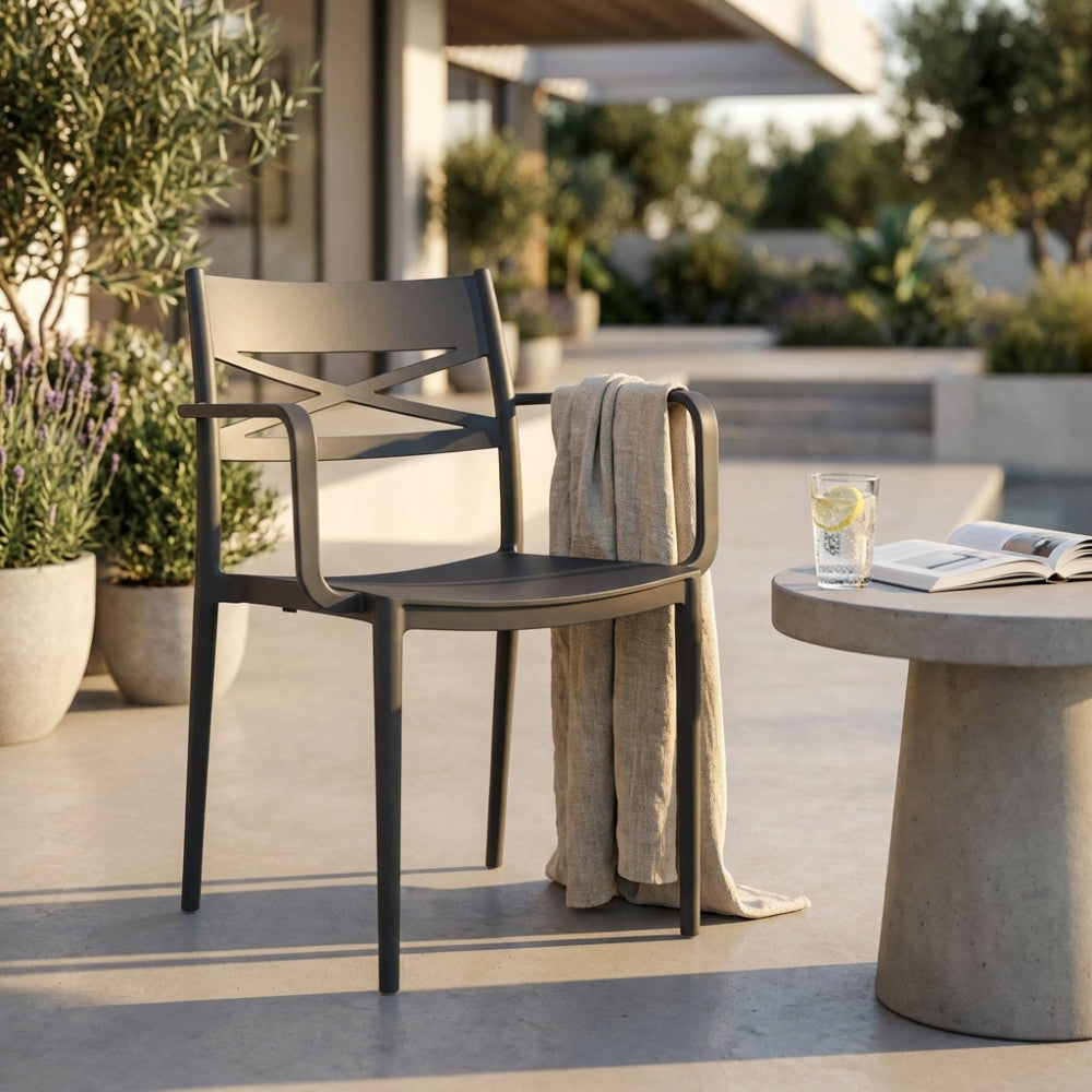 Poltrona moderna Darleen con braccioli su una terrazza in cemento, illuminata dalla luce naturale del tramonto.