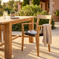 Poltrona Delhi in teak e wicker ambientata all'aperto accanto a un tavolo in legno.