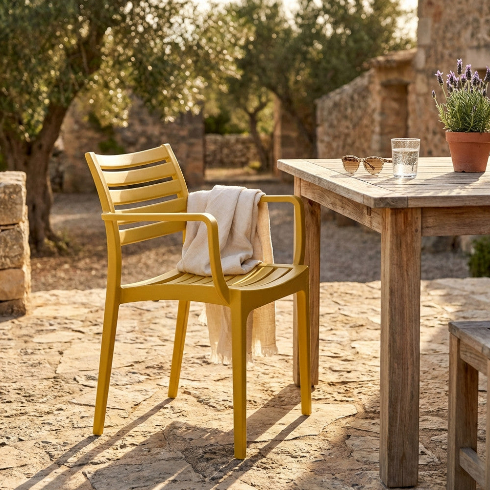Poltrona Eveline in polipropilene giallo posizionata all'aperto su un patio in pietra, accanto a un tavolo in legno rustico.