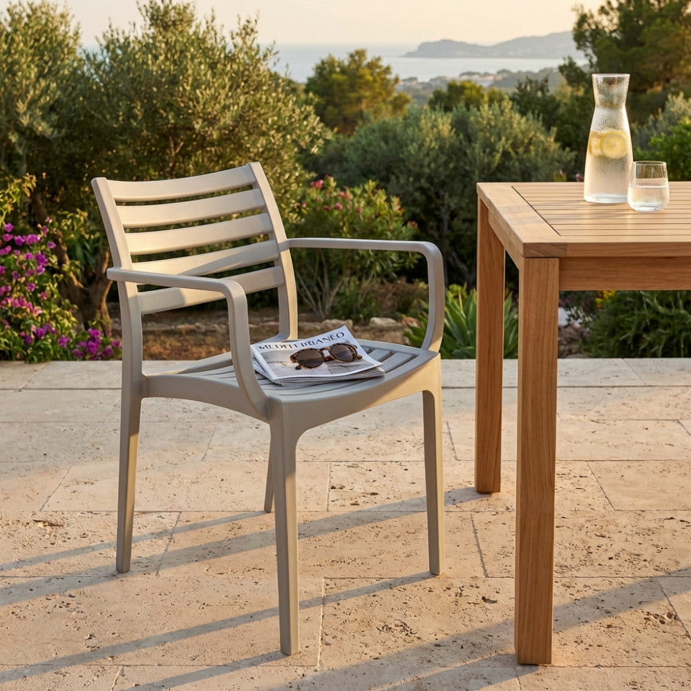 Poltrona Eveline in polipropilene grigio ambientata all'aperto su una terrazza in pietra, accanto a un tavolo in legno di teak.
