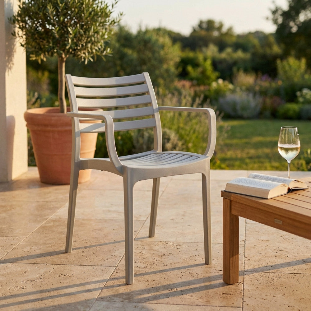 Vista ravvicinata della Poltrona Eveline grigia in un giardino lussuoso, con un calice di vino e un libro sul tavolo adiacente.