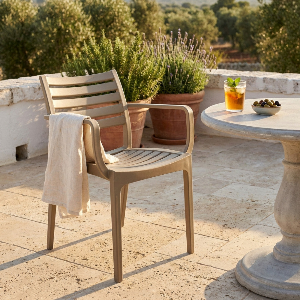 Poltrona premium color tortora Eveline ambientata su un patio in pietra con piante mediterranee.