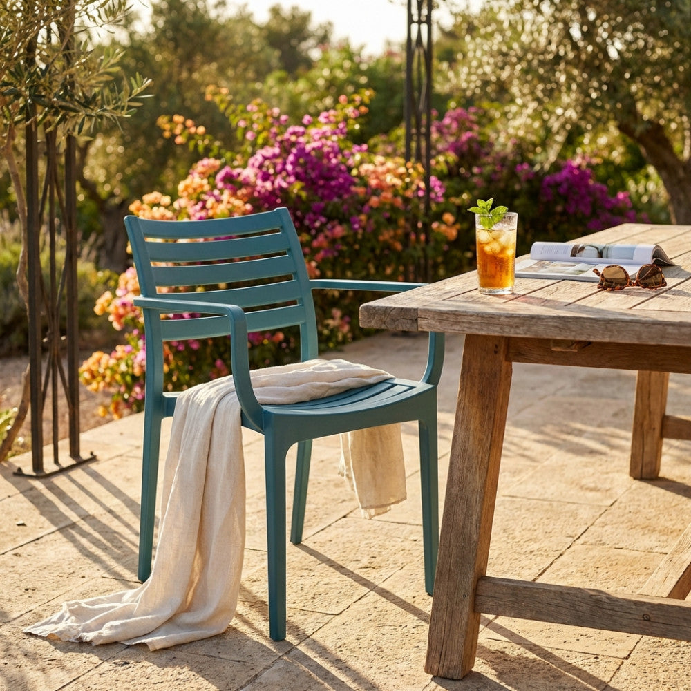 Poltrona Eveline verde con un telo in lino appoggiato, ambientata su un patio in pietra con fiori sullo sfondo.
