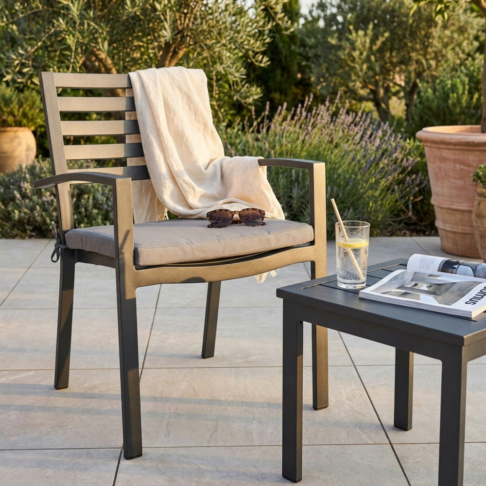 Poltrona Formentera in alluminio antracite ambientata in un giardino lussuoso con plaid e occhiali da sole.