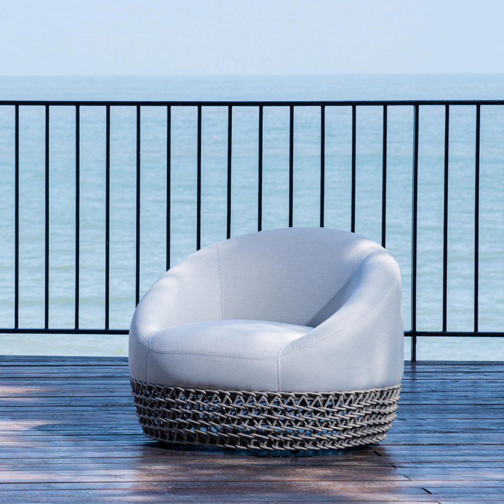 Poltrona girevole da esterno posizionata su una terrazza in legno con vista panoramica sul mare.