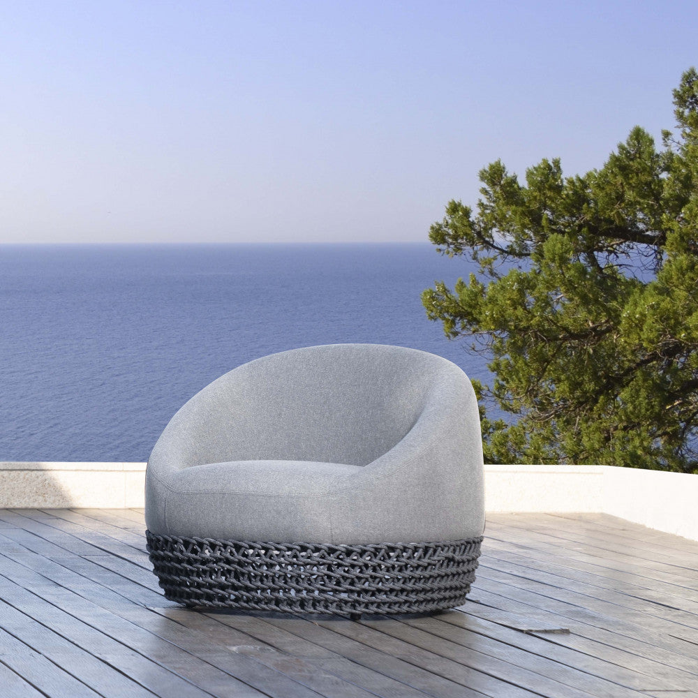 Poltrona girevole Lafayette posizionata su una terrazza in legno con vista panoramica sul mare.