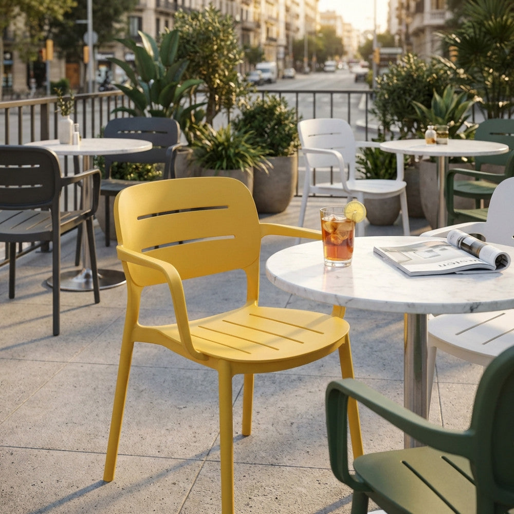 Poltrona di design Giselle in finitura gialla, posizionata in un elegante caffè all'aperto con tavolini in marmo.