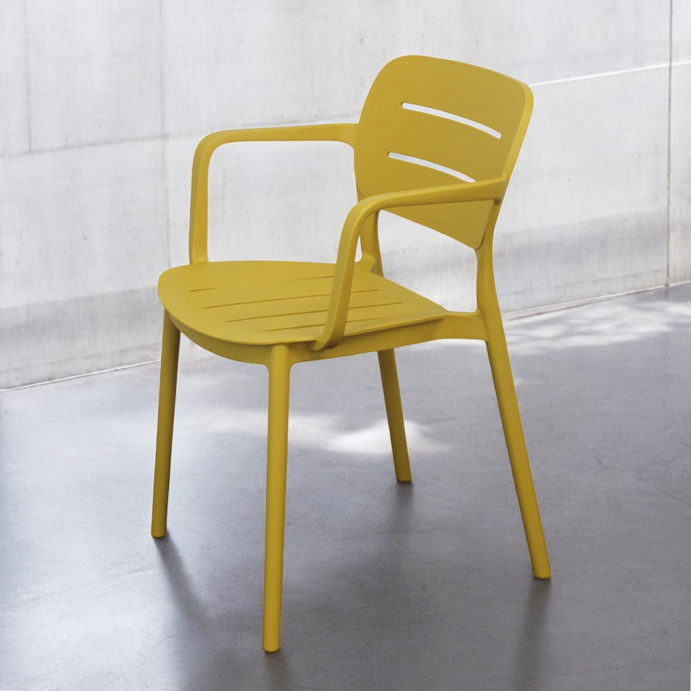 Poltrona moderna Giselle gialla illuminata dalla luce naturale in un ambiente interno minimalista con pareti in cemento.