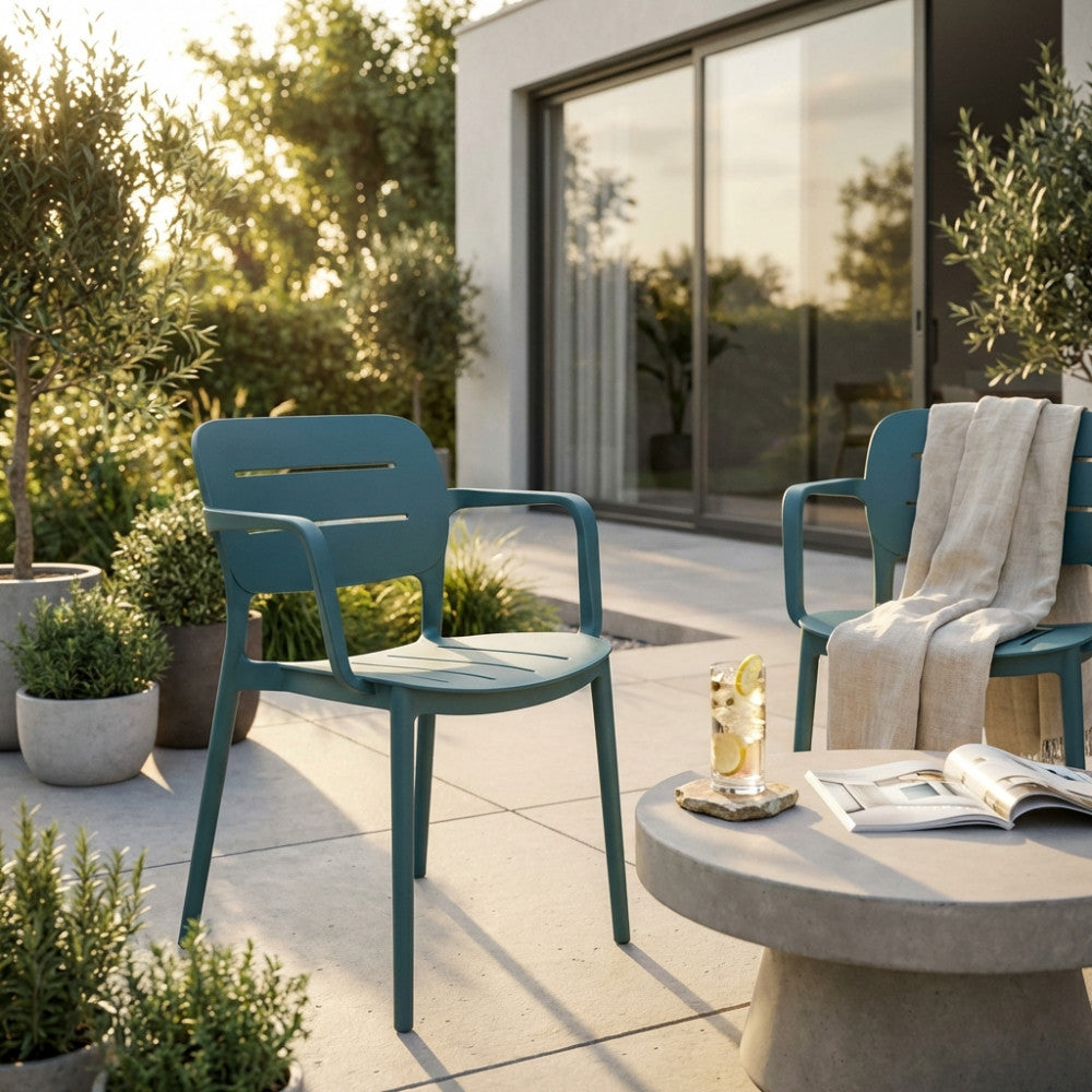 Coppia di poltrone Giselle verde petrolio su un patio moderno al tramonto, vicino a un tavolino rotondo.
