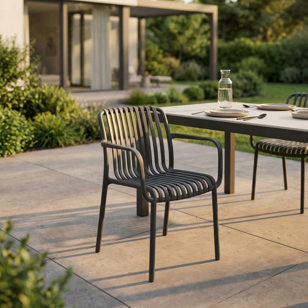 Poltrona Giuly color taupe disposta attorno a un tavolo da pranzo moderno in un giardino elegante.