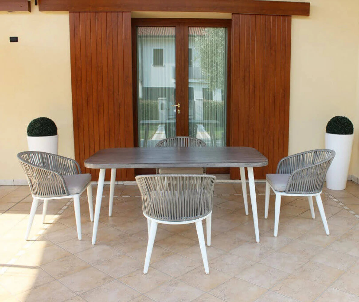 Poltrona Granada Grigia con intreccio in polyrattan e struttura in alluminio, cuscini sfumati, per salotto da esterno, ambientata con tavolo e sedie in veranda