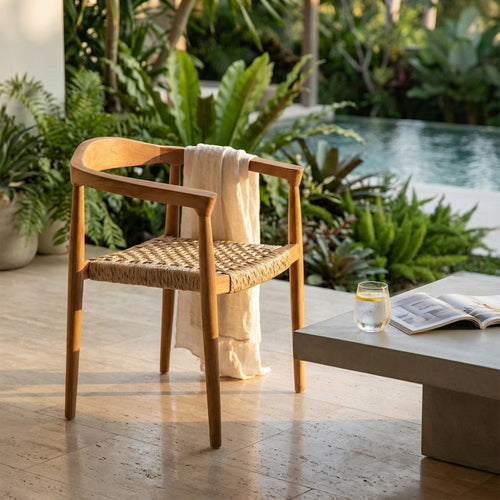 Poltrona Harvard in teak con seduta intrecciata situata all'aperto vicino a una piscina, allestita con un asciugamano e un tavolino in cemento.