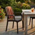 Poltrona Indiana in wicker marrone ambientata in un giardino elegante con tavolo in legno e coperta in terracotta.