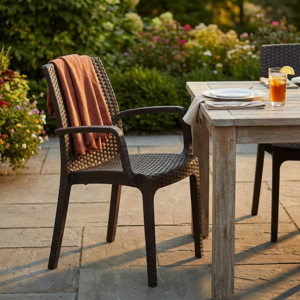 Poltrona Indiana in wicker marrone ambientata in un giardino elegante con tavolo in legno e coperta in terracotta.