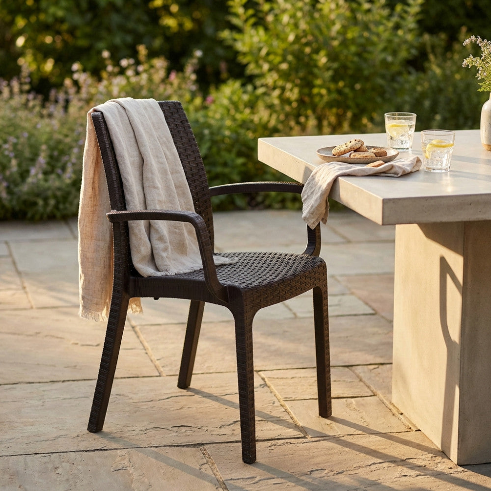 Poltrona Indiana con braccioli posizionata su un patio in pietra accanto a un tavolo in cemento dal design contemporaneo.