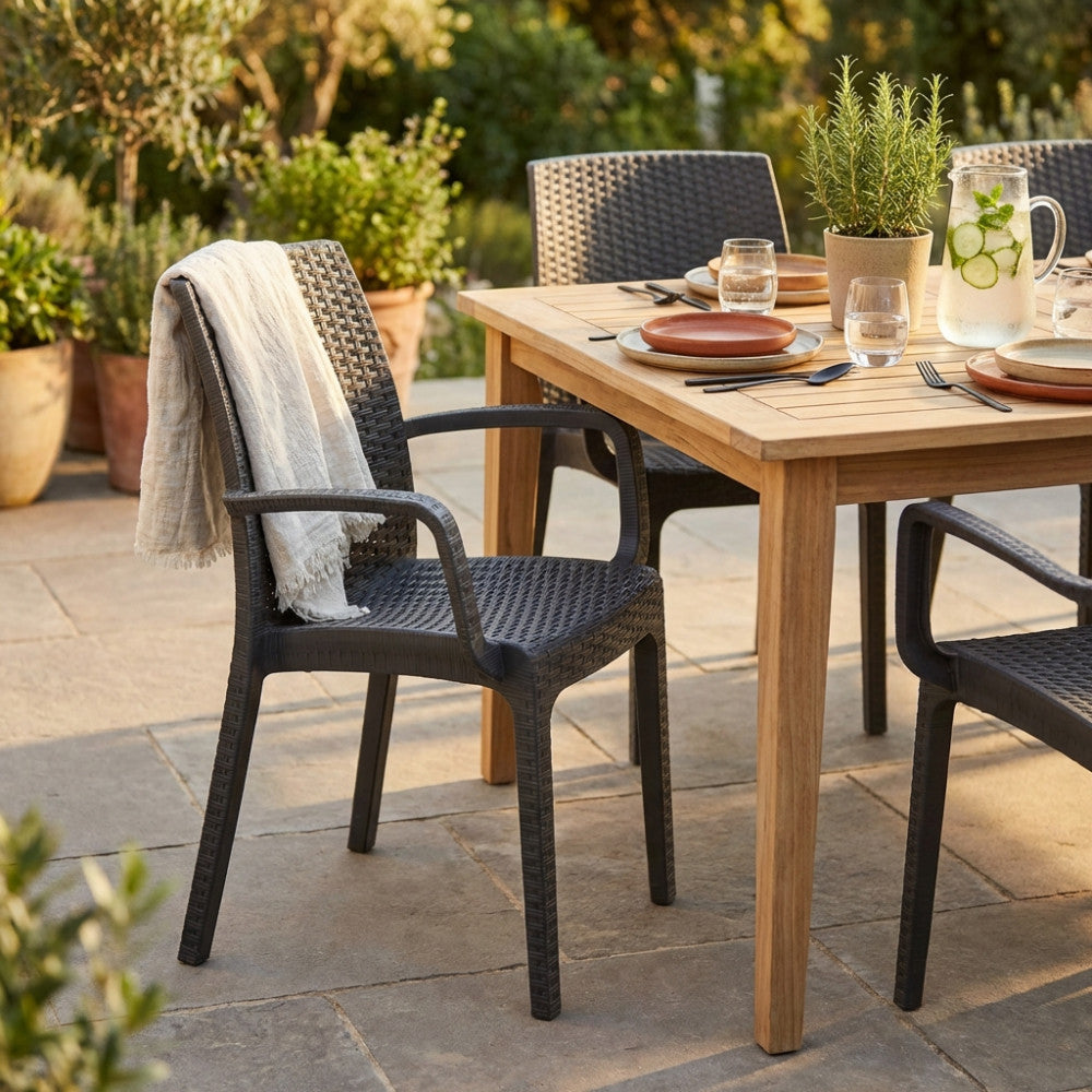 Poltrona Indiana in wicker taupe ambientata in un giardino elegante accanto a un tavolo in teak.