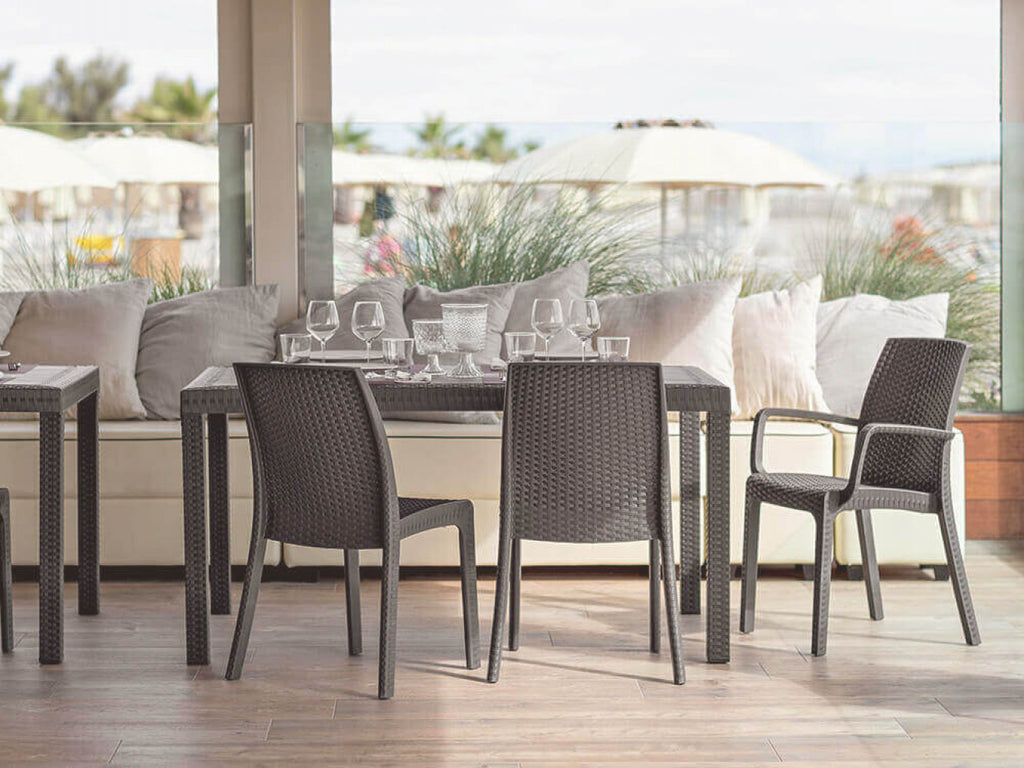 Set di poltrone Indiana in wicker taupe disposte attorno a un tavolo da pranzo in un patio coperto di lusso.