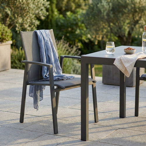 Poltrona Maili in alluminio e textilene antracite, ambientata all'aperto su una terrazza in pietra con un telo azzurro appoggiato.