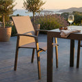 Poltrona Maili in alluminio e textilene color taupe ambientata su una terrazza esterna al tramonto, affiancata a un tavolo coordinato.