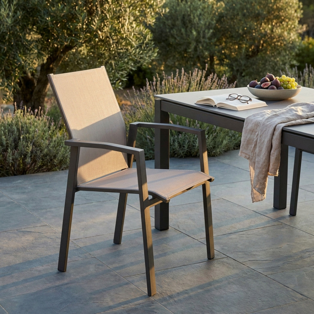 Dettaglio della poltrona Maili con braccioli inserita in un contesto outdoor elegante, vicino a un tavolo apparecchiato con frutta e calici.