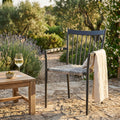 Poltrona Martinica in alluminio e wicker antracite ambientata in un giardino rustico con tavolino in legno e calice di vino.