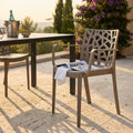 Poltrona Matrix in polipropilene tortora posizionata su un patio in pietra illuminato dal sole accanto a un tavolo da pranzo moderno.