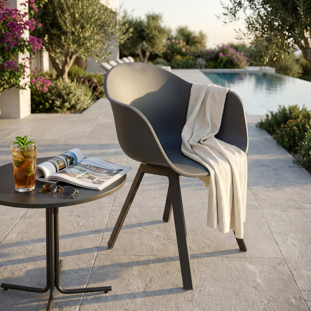 Poltrona Maui grigio antracite in plastica e alluminio, ambientata a bordo piscina con un plaid chiaro e un tavolino da caffè.