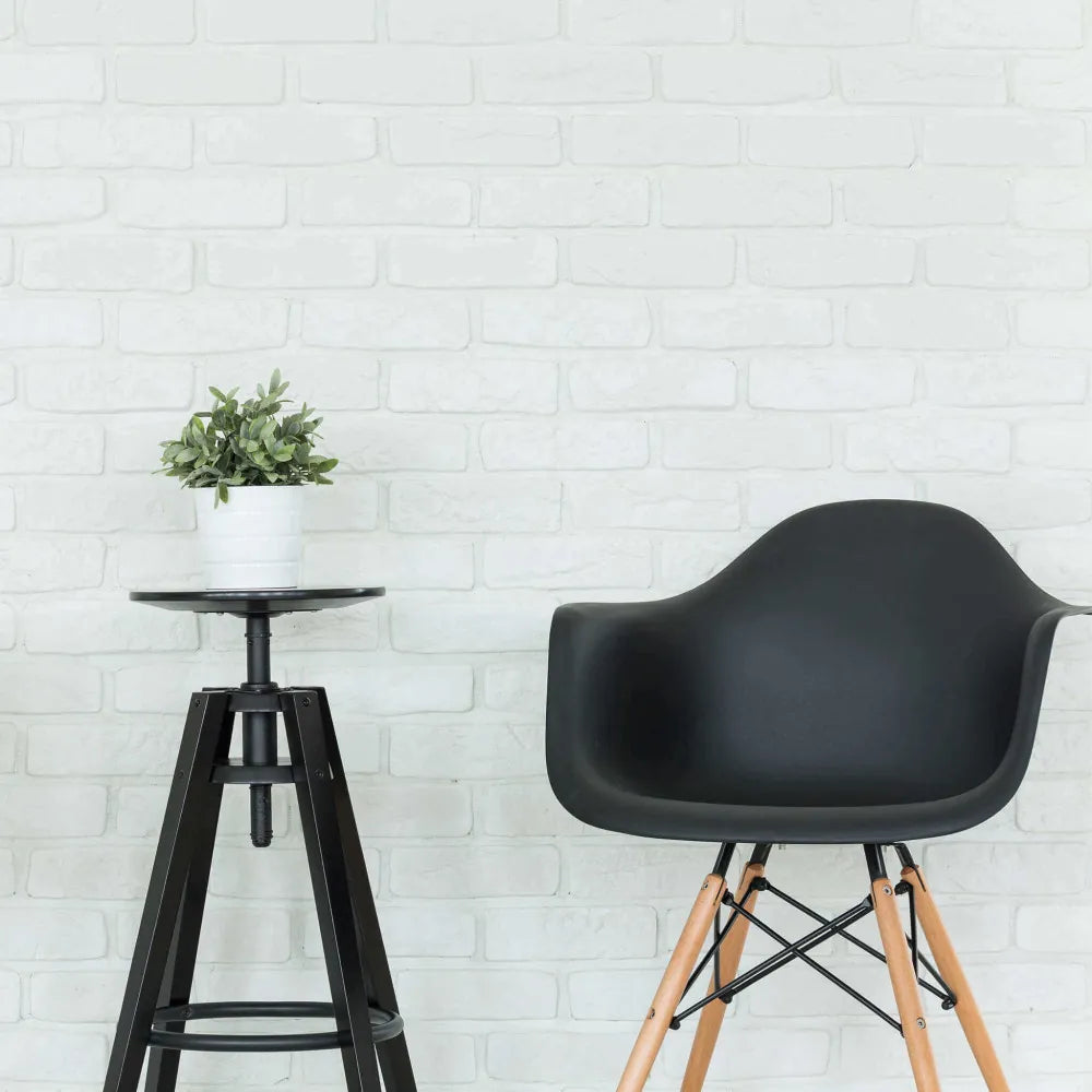 Poltrona Moritz nera con braccioli, seduta in plastica ABS nera e gambe in legno naturale e metallo, abbinata con sgabello industriale