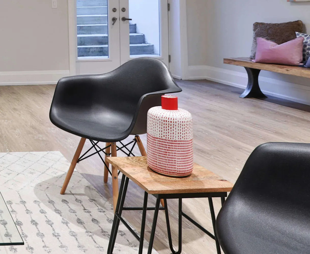 Poltrona Moritz nera con braccioli, seduta in plastica ABS nera e gambe in legno naturale e metallo, ambientata in un soggiorno in stile industriale