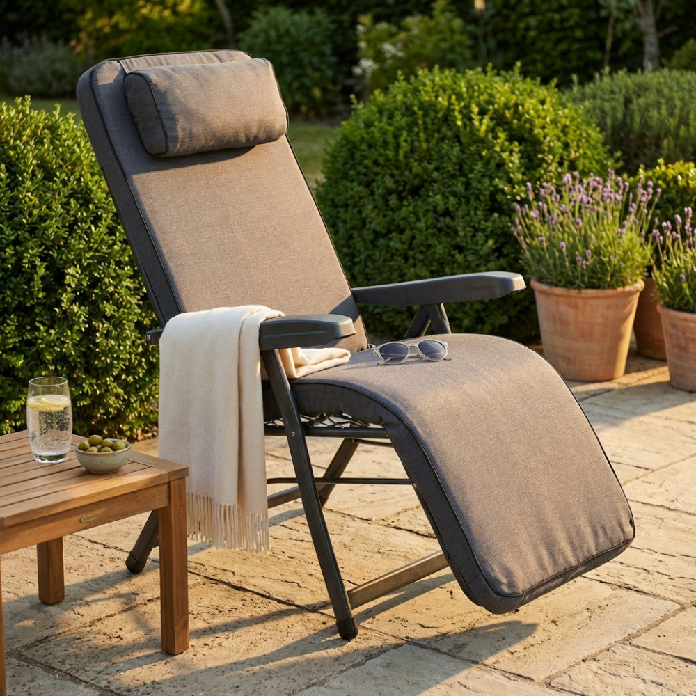 Poltrona relax Paradiso grigia in tessuto e acciaio ambientata su un patio in pietra con coperta chiara.