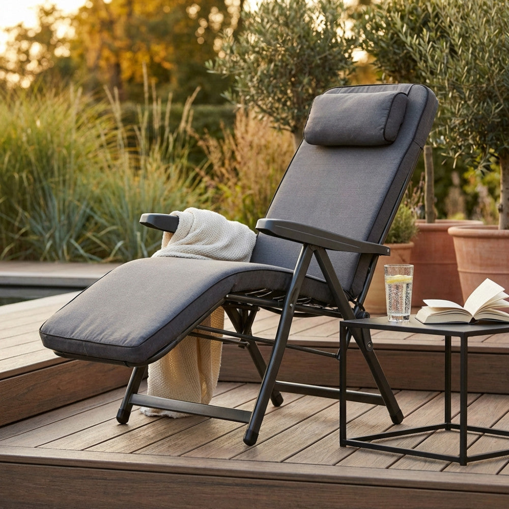 Poltrona relax grigia posizionata su un deck in legno a bordo piscina con libro e bicchiere.