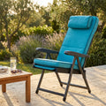 Poltrona relax Paradiso azzurra in tessuto e acciaio, ambientata in un giardino soleggiato accanto a un tavolino in legno.
