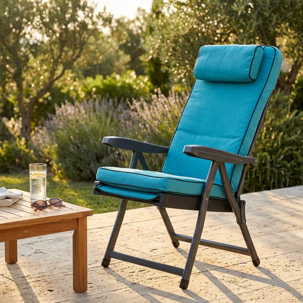 Poltrona relax Paradiso azzurra in tessuto e acciaio, ambientata in un giardino soleggiato accanto a un tavolino in legno.
