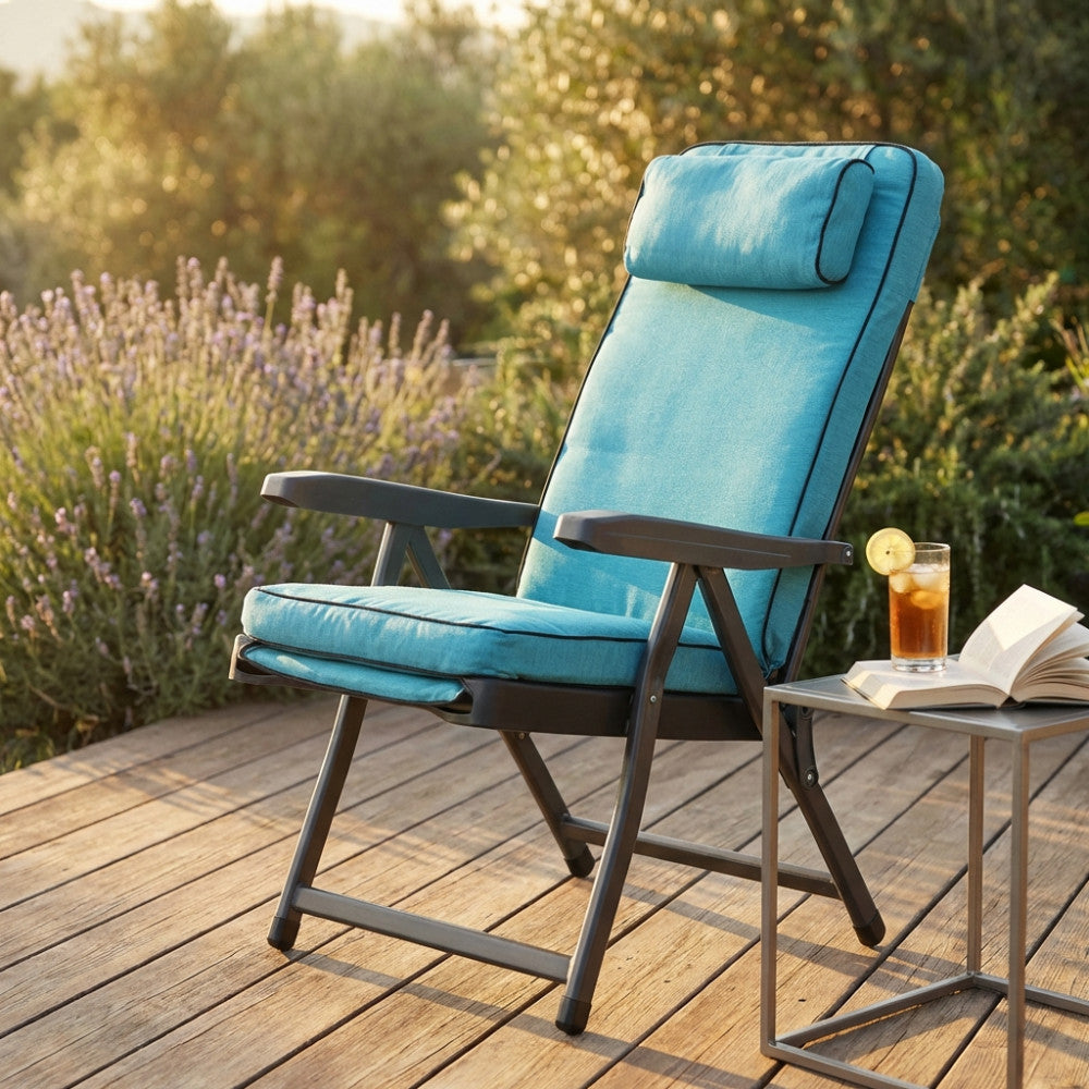 Dettaglio della poltrona relax Paradiso su una terrazza in legno, con un drink e un libro sul tavolino laterale.