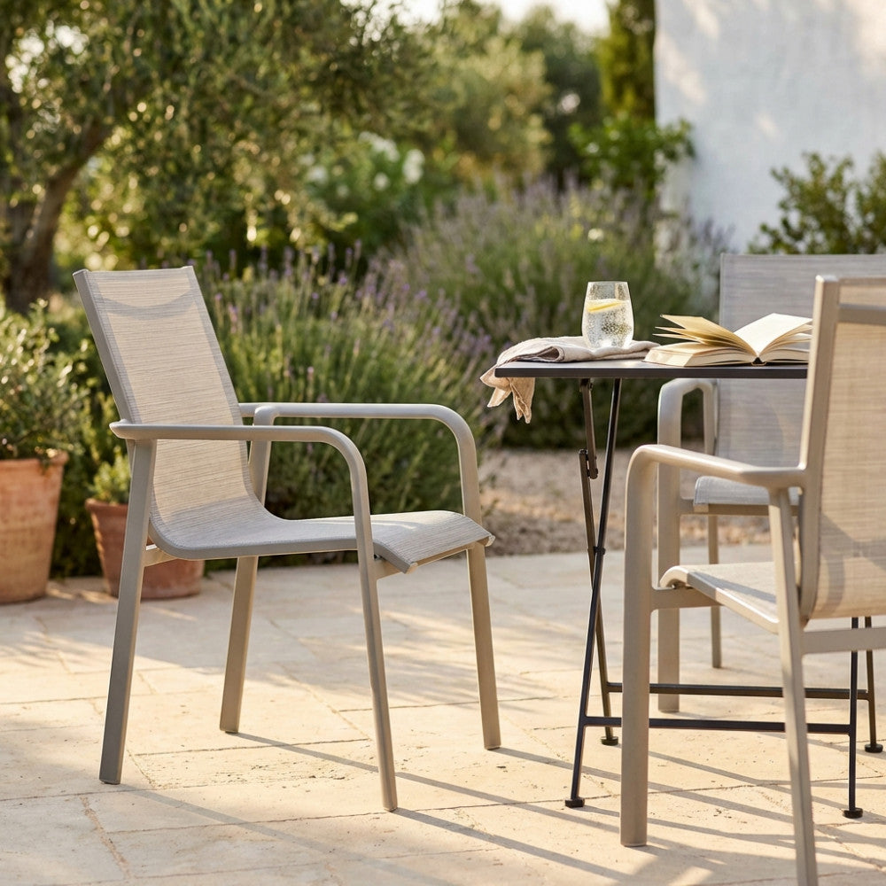 Due poltrone outdoor grigio sabbia in alluminio e poliestere disposte attorno a un tavolino nero su un patio in pietra, illuminate dalla luce naturale.