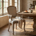 Poltrona Romy in tessuto grigio e legno intagliato, ambientata in una sala da pranzo rustica vicino a un tavolo in legno.