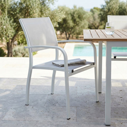 Poltrona Savannah in alluminio bianco ambientata in un patio soleggiato accanto a un tavolo in teak.