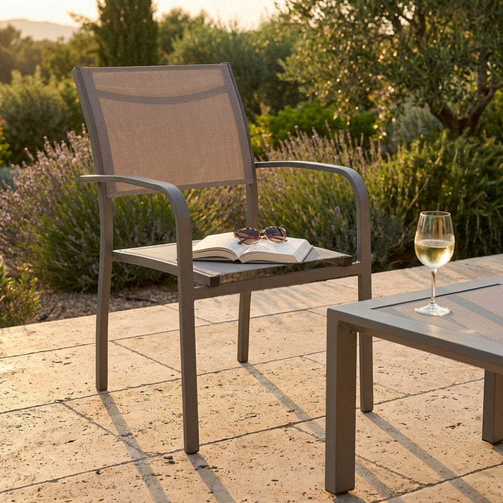 Poltrona in alluminio Savannah color taupe ambientata in un giardino al tramonto con un libro e un bicchiere di vino.