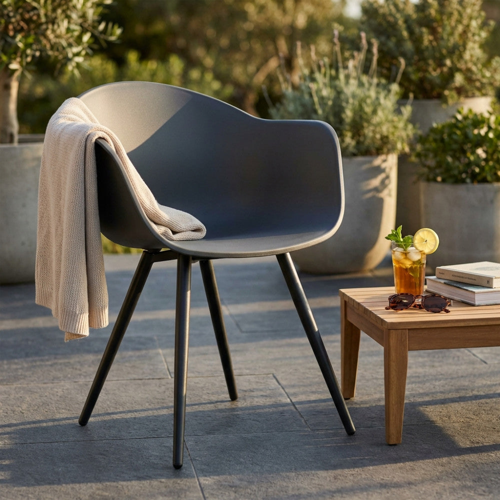 Poltrona Sestriere in plastica e alluminio decorata con un plaid neutro, situata su un patio in pietra vicino a un tavolino.
