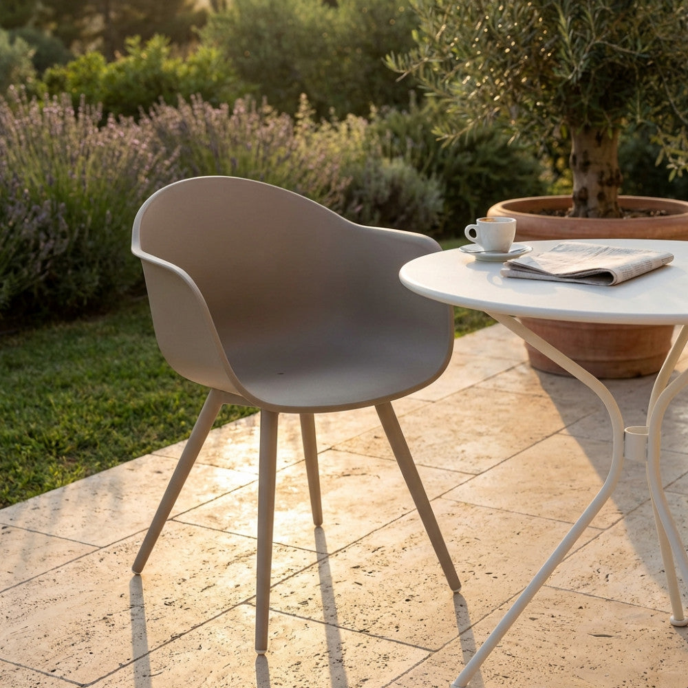 Poltrona Sestriere con braccioli posizionata su un patio in travertino accanto a un tavolino bianco da esterno.