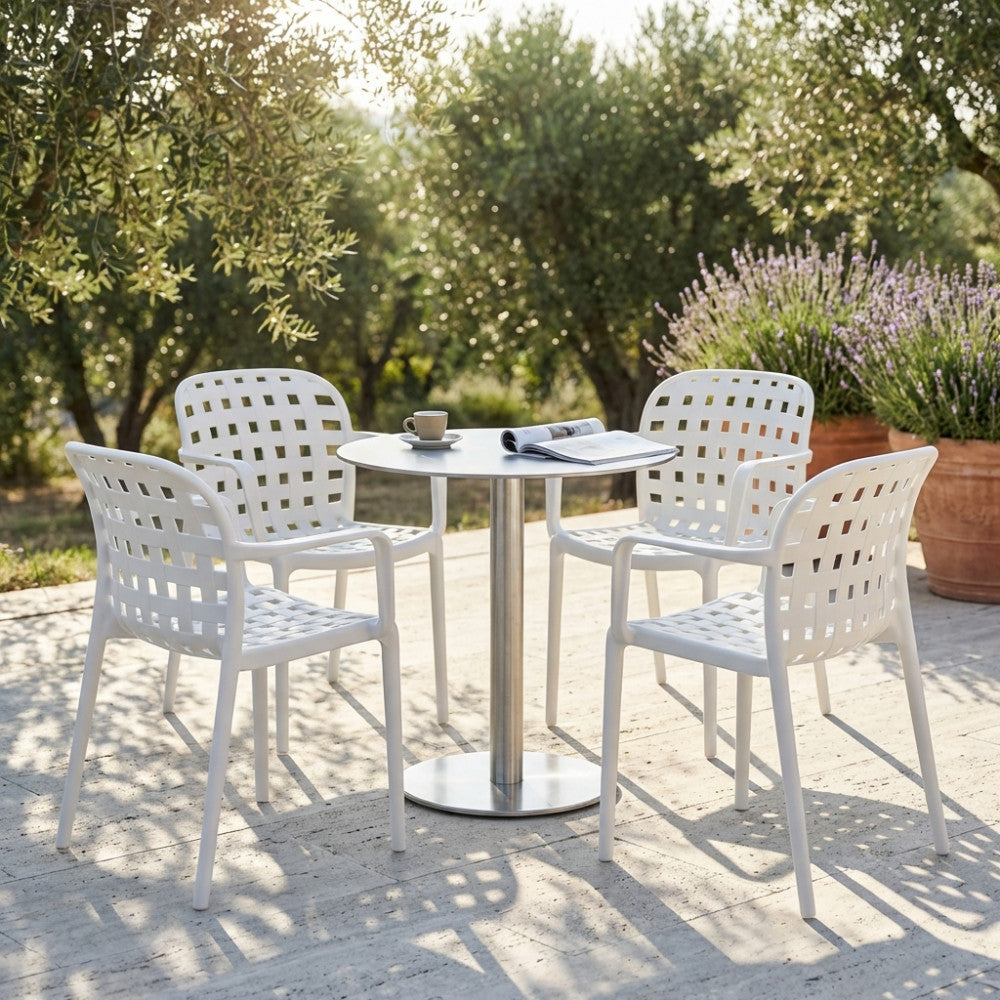 Set di quattro poltrone Sharon bianche attorno a un tavolo rotondo in metallo, in un giardino mediterraneo con ulivi.