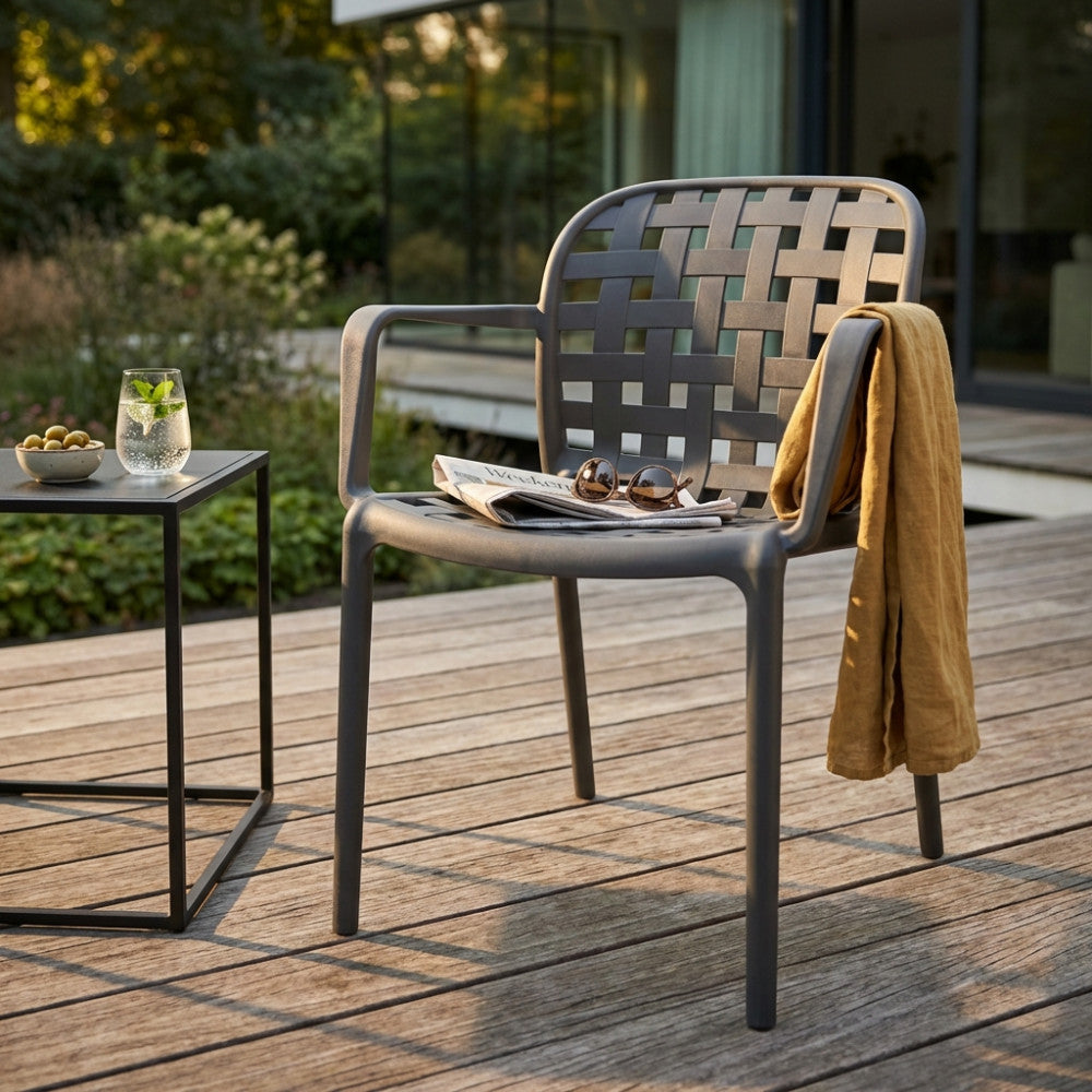 Poltrona Sharon color taupe con motivo a intreccio posizionata su una terrazza in legno con tavolino minimalista.
