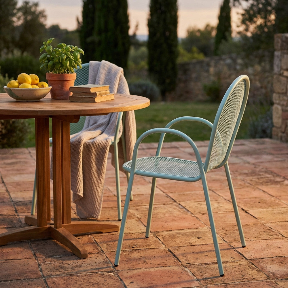 Poltrona Sheffield con braccioli posizionata su un patio in cotto vicino a un tavolo in legno di teak.